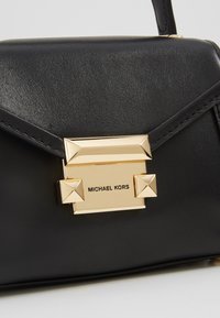 Sac à main en cuir noir avec fermoir rectangulaire doré gravé "MICHAEL KORS" et clous pyramides sur le rabat avant.