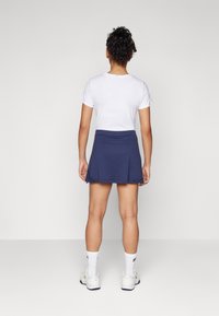 Marineblauwe rok met plooien, gecombineerd met een wit shirt met korte mouwen. Gezicht vanuit de achterkant, met een geweven stof en sportieve sokken.