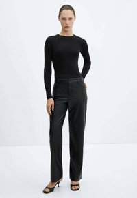 Top nero a maniche lunghe abbinato a pantaloni in pelle nera a vita alta, con un design aderente e una texture liscia e lucida. Tacchi neri completano l'outfit.