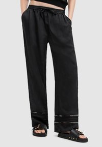 Zwarte, lichtgewicht broek met een elastische tailleband, zijzakken en contrasterende afwerking op de zoom. Gecombineerd met stevige slide-sandalen.