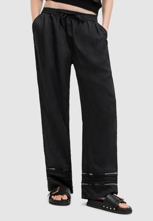 Zwarte, lichtgewicht broek met een elastische tailleband, zijzakken en contrasterende afwerking op de zoom. Gecombineerd met stevige slide-sandalen.