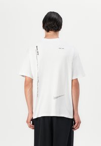 Hvid bomulds t-shirt med korte ærmer, prydet med et trykt Nike-logo og tekst på ryggen. Glat tekstur med en afslappet pasform.