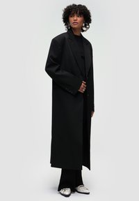 Blazer nero over-size con un solo bottone, ampi rever e taglio sartoriale; abbinato a un top nero a coste e pantaloni svasati, con scarpe dettagli argentati.