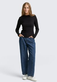 Zwarte geribbelde lange mouw top met een ronde halslijn, gecombineerd met hoge blauwe denim wijde jeans en witte sneakers.