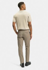 Beige rippad polo med korta ärmar, kompletterad med ljusbruna figurnära byxor och svarta skor, sedd bakifrån.