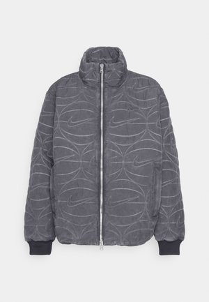 Giubbotto imbottito grigio trapuntato con colletto alto, zip frontale e polsini elasticizzati. Presenta il logo Nike in rilievo e un motivo a linee curve.