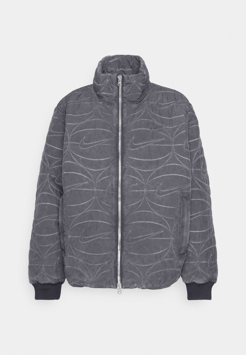 Giubbotto imbottito grigio trapuntato con colletto alto, zip frontale e polsini elasticizzati. Presenta il logo Nike in rilievo e un motivo a linee curve.