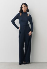 Top a maniche lunghe color blu navy con spalle scoperte abbinato a pantaloni blu navy a vita alta e con gambe larghe. Tessuto liscio con dettagli sartoriali.
