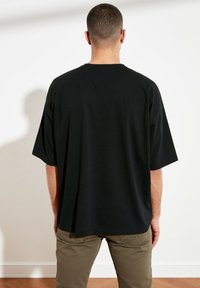 Czarna, oversize koszulka wykonana z bawełny, z krótkimi rękawami i okrągłym dekoltem, widok z tyłu. W połączeniu z khaki spodniami.