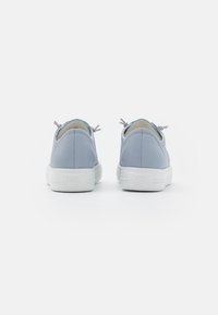 Un paio di sneakers in pelle azzurro chiaro con suole bianche spesse, viste da dietro su uno sfondo bianco uniforme.