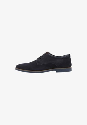 Zapato de vestir negro de ante con una textura suave, punta redonda y cordones finos. Presenta una suela de goma marrón en contraste y detalles cosidos.
