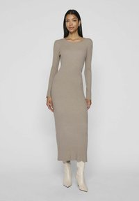 Long-sleeve ribbed dress in light taupe, fitted design, round neckline, reaching mid-calf, paired with cream-colored high-heeled boots.