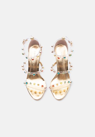 Ζευγάρι χρυσά σανδάλια με διάφανα λουράκια διακοσμημένα με πολύχρωμους στρογγυλούς πολύτιμους λίθους, με επίπεδη σόλα και κούμπωμα στον αστράγαλο, σε θέα από πάνω.