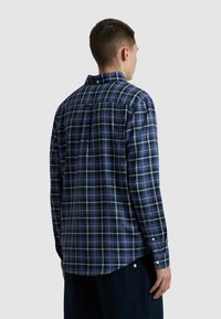 Camicia a maniche lunghe a quadri blu navy con motivi a scacchi blu, verdi e bianchi. Presenta uno yoke posteriore e polsini con bottoni. Materiale in cotone morbido.