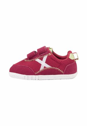 Zapatilla deportiva infantil roja con suela blanca, dos tiras de velcro, tejido de malla y costura blanca en forma de "X" en el lateral, vista desde el interior.