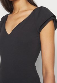 Femme portant un top noir cintré avec un col en V et des manches courtes légèrement bouffantes.