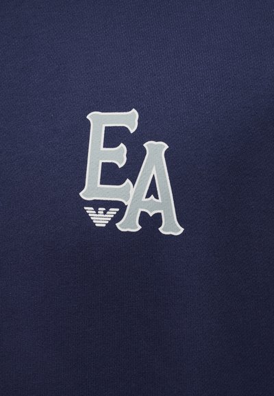 Σκούρο μπλε ύφασμα με μεγάλους ανοιχτό γκρι χαρακτήρες "E" και "A" τυπωμένους κοντά, συνοδευόμενους από ένα μικρό λευκό στυλιζαρισμένο έμβλημα κάτω από τα γράμματα.