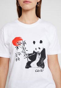 Vit bomullströja med en svart och vit pandaillustration som håller i bambu, med en röd accent och texten "GO SLOW" under.