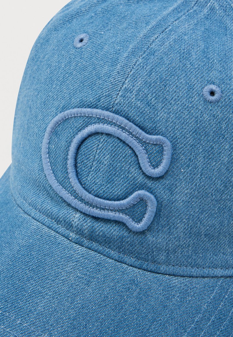 Denim cap in light blue, featuring a textured surface. Displays a large, embroidered letter "C" in matching thread on the front.