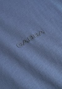 Modra bombažna tkanina z diskretno teksturno površino, s črnim embosiranim logotipom "GABBA", ki je prominently v središču.
