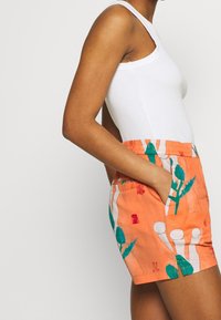 Oranga shorts i tyg har en blommig och abstrakt design i teal och röd. De har ett elastiskt midjeband och sidofickor.