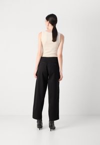 Beige ermeløs topp kombinert med høy midje svarte vidde bukser. Svart hæl støvler fullfører antrekket. Minimalistisk design, glatte teksturer.