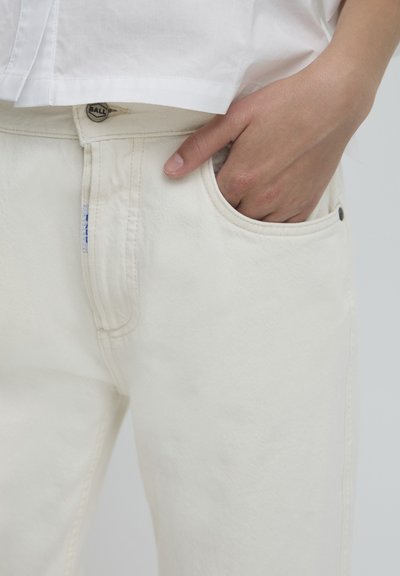 Un jean en denim blanc présente un design classique avec jambe droite, des coutures visibles, une poche avant et un bouton en métal.