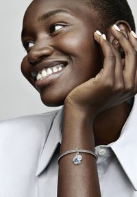 Bracciale in argento con un ciondolo floreale blu e un'etichetta rotonda, caratterizzata da un'incisione. Il bracciale presenta un design testurizzato e una chiusura.