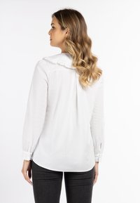 Weißes Blusenshirt mit langen Ärmeln, gerafftem Kragen und Knopfmanschetten. Hat einen geschwungenen Saum hinten und eine weiche, glatte Textur.