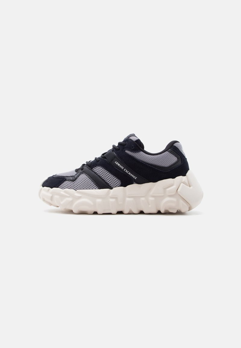 Μαύρο και γκρι αθλητικό παπούτσι από δίχτυ με άσπρη, χοντρή σόλα που έχει μοτίβο στο πέλμα και λογότυπο «Armani Exchange» στο πλάι.