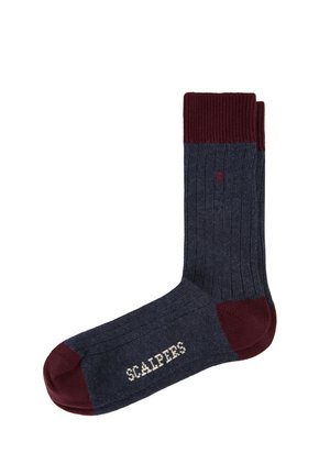 Calcetín acanalado gris oscuro con puño, talón y puntera en marrón granate, con un pequeño logo de calavera y el texto "Scalpers" en la suela.