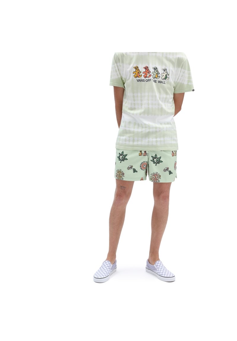 T-shirt tie-dye vert avec des graphiques de lapin, associé à un short vert clair orné de motifs floraux. Tenue complétée par des chaussures sans lacets à carreaux.