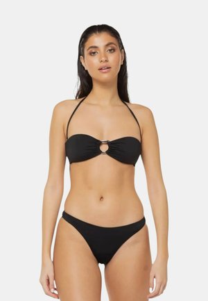 Donna che indossa un bikini nero a due pezzi con un top senza spalline caratterizzato da un dettaglio a anello metallico frontale e sottili spalline a collo halter.
