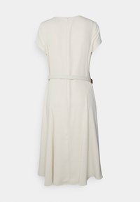 Cläddress i krämfärg med korta ärmar, midja som är åtstramad och en dragkedja bak. Tyget är slätt med subtila veck vid kjolen.