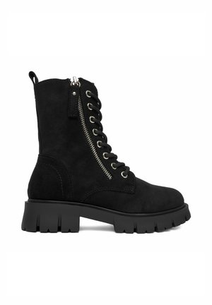 Czarny zamszowy but bojowy z grubą podeszwą z wypustkami, sznurowaniem z przodu i bocznym zamkiem błyskawicznym biegnącym równolegle do dziurek na sznurówki.