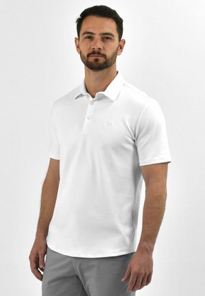 Witte polo met een drieknops sluiting, zachte textuur, korte mouwen en een subtiele logo op de borst, gecombineerd met lichtgrijze shorts.