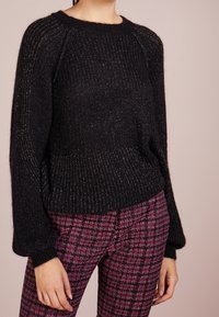 Suéter negro de punto con textura acanalada, mangas abullonadas y cuello redondo. Combinado con pantalones de estampado rosa y negro.