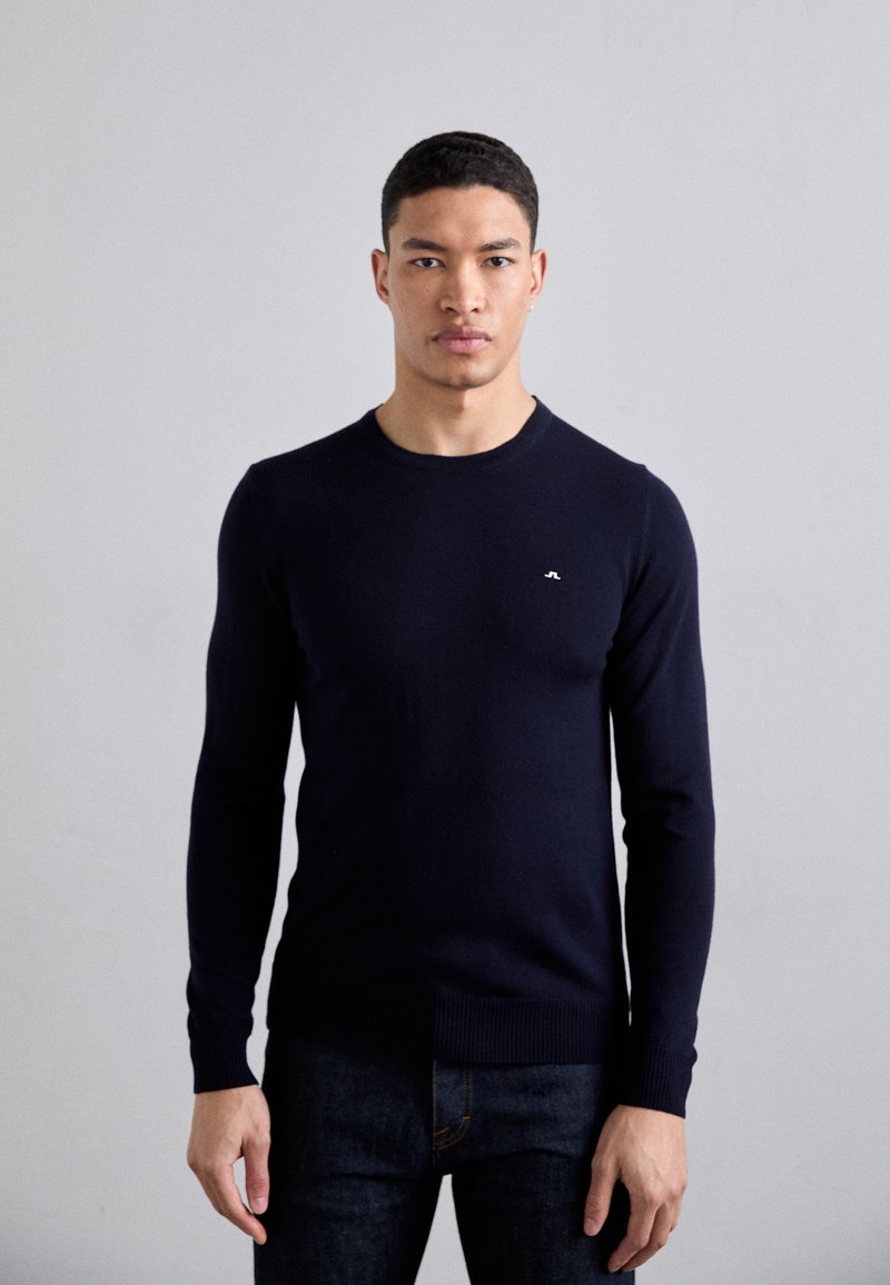 Navyblauer Pullover mit langen Ärmeln in enganliegendem Design, rundem Hals und gerippten Bündchen. Kleines Logo-Detail auf der Brust, aus weichem Material hergestellt.