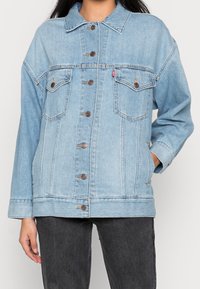 Ljusblå denimjacka med knäppning fram, två bröstfickor och en avslappnad passform. Har en krage och sömnadsdetaljer.