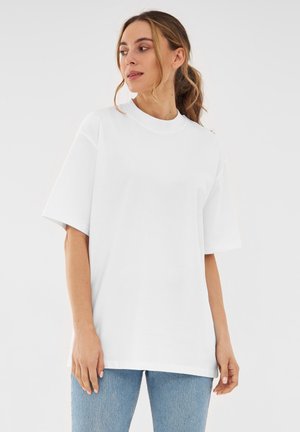 Witte oversized t-shirt met korte mouwen, ronde hals, gemaakt van katoen, gladde textuur, losse pasvorm, gedragen met lichtblauwe spijkerbroek.