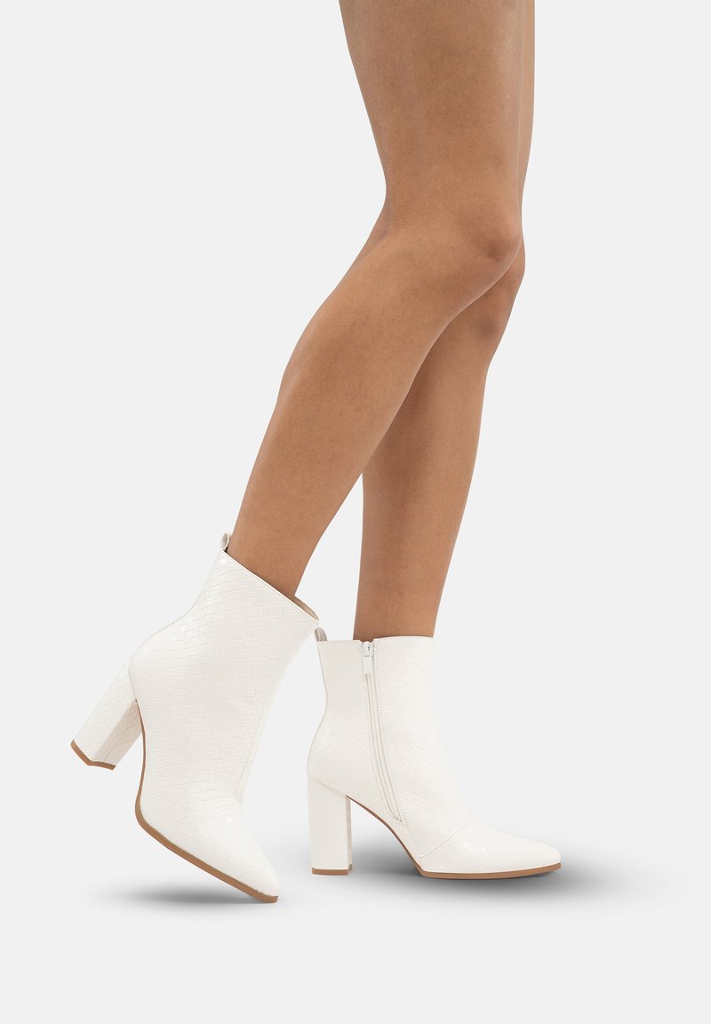 Botas blancas hasta el tobillo con una superficie texturizada, tacones de bloque y una cremallera lateral. Acabado suave con un patrón geométrico y un diseño de punta afilada.