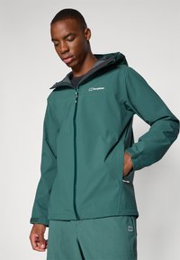 Teal vandtæt jakke lavet af struktureret stof, med en frontlynlås, hætte, elastiske manchetter og "berghaus"-logoet på brystet.