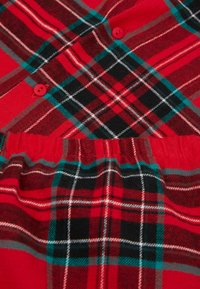 Červená kostkovaná látka se směsí červených, černých a tyrkysových vzorů. Obsahuje červené knoflíky a elastický pas na spodní části.