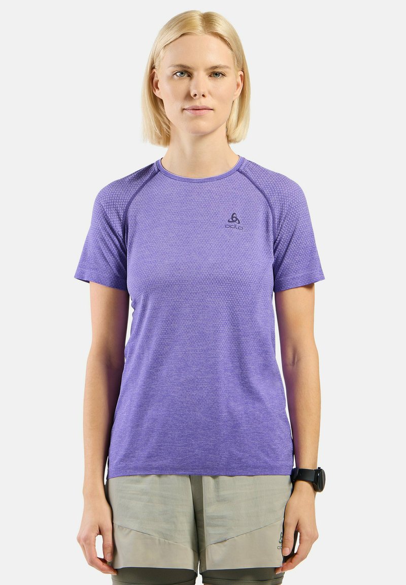 Haut de sport violet à manches courtes avec un motif texturé, col rond et logo sur la poitrine. Le matériau semble léger et respirant.