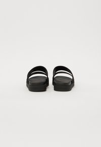 Sandale negre cu două curele late și talpă plată. Fabricate din material ușor, cu o textură netedă și un design minimalistic.