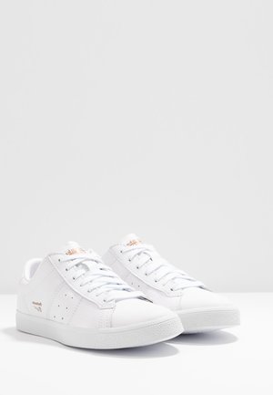 Valkoiset urheilukengät, joissa on sileä nahkapinta, tasaiset nauhat, määrätyt sivut, kumipohjat ja huomaamattomat brändivaihtoehdot.