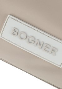 Beige nylon pouch med et hvidt gummilogo med præget tekst. Overfladen er glat med synlige søm detaljer.