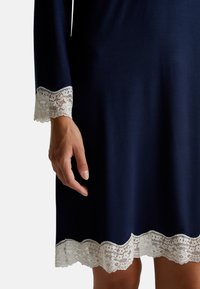 Abito blu navy con maniche lunghe. Presenta bordi in pizzo bianco ai polsini e all'orlo. Texture morbida, taglio dritto e dettagli in pizzo scallop.