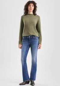 Groen gebreid sweater met een ronde halslijn en textuurdetails, gecombineerd met uitlopende blauwe spijkerbroek en donkere enkellaarzen.