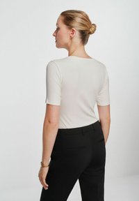 Dopasowana bluzka z krótkim rękawem w jasnobeżowym prążkowanym materiale, zestawiona z czarnymi spodniami z kieszeniami bocznymi i gładką fakturą.